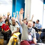 Conference participants with smiles and raised hands.